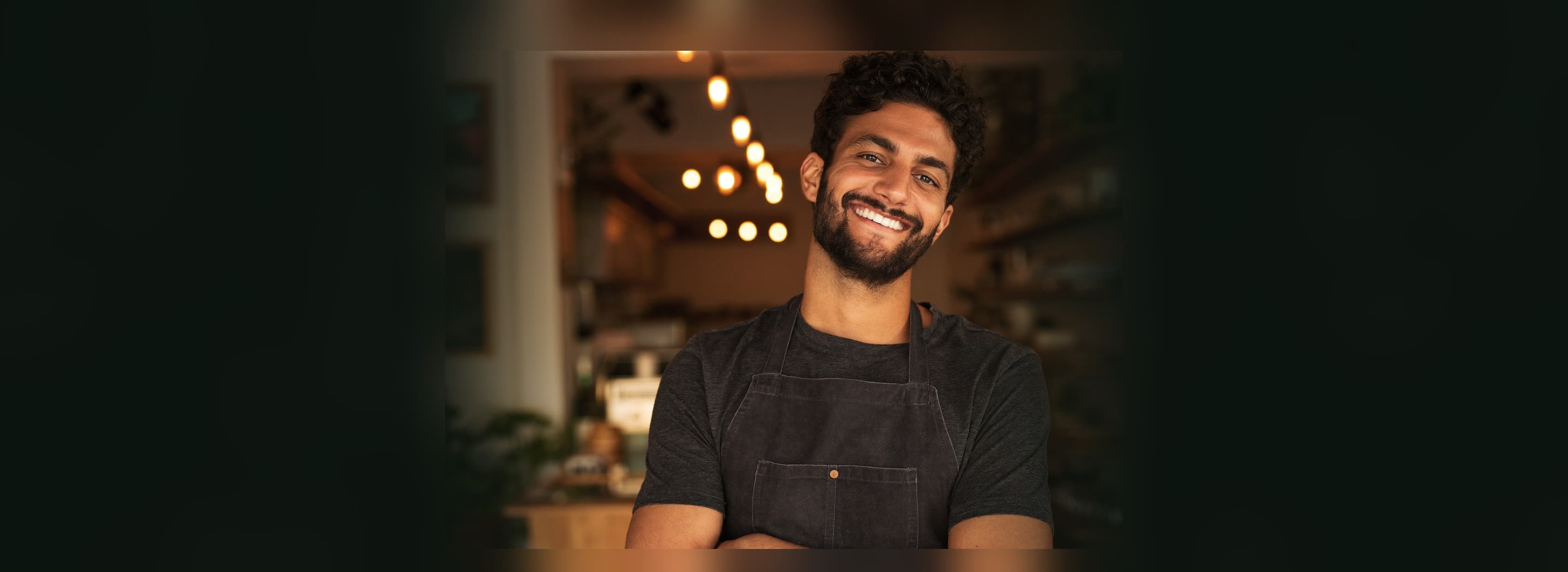 Empreendedor de avental, braços cruzados, sorrindo em seu negócio